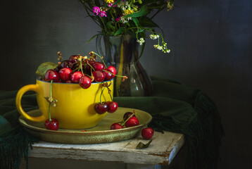 Wall Mural - Still life with ripe cherries in a large yellow cup and a bouquet of meadow flowers.