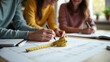 © Nima - Measuring tape for interior design planning. Three people collaborate on architectural plans, using measuring tapes and notebooks, highlighting teamwork and creativity in design.