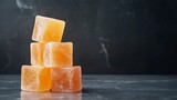 Cannabis, gummies. A stack of amber-colored sugar cubes is elegantly arranged on a dark surface, showcasing their translucent texture and simplicity.