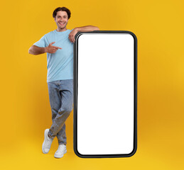 Poster - Check This Website. Smiling male leaning on smart phone with white blank screen, showing device and pointing finger at gadget with empty free copy space for mock up, recommending app, full body length