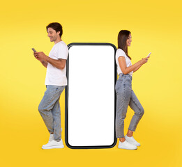 Wall Mural - Great App. Excited Couple Leaning On Big Smartphone With Blank White Screen Using Cell Phones, Cheerful Guy And Lady Chatting On Social Media, Standing On Yellow Orange Background, Mock Up, Full Body