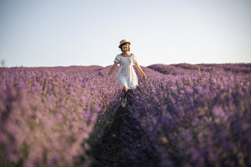 Wall Mural - Lavender field happy girl in white dress with hat runs through a lilac field of lavender. Aromatherapy travel