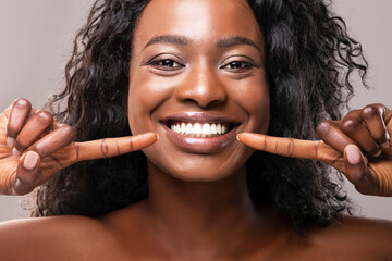 teeth alignment and whitening concept. happy african american girl pointing at her wide smile with t