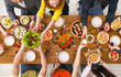 © Prostock-studio - People eat healthy meals at festive table served for party. Friends celebrate with organic food on wooden table top view. Happy company having lunch, taking salad dish