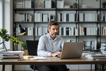 Poster - A man focused on his laptop in a contemporary office surrounded by neatly organized books on shelves