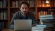 © IgorImageDoc - The image shows a young man sitting at a wooden table with a laptop in front of him. He is wearing a gray sweater and has a beard.