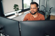 © Zamrznuti tonovi - Smiling businessman wearing headset working with dual screen computer in office