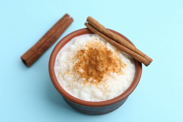 Wall Mural - Delicious rice pudding with cinnamon sticks on light blue background, closeup