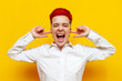© Богдан Маліцький - young short-haired red-haired angry girl screams and covers her ears on a yellow isolated background, irritated hipster woman with piercing suffers from noise problem
