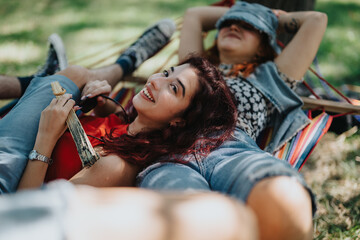 Wall Mural - Two joyful friends sharing a hammock in a green park on a sunny day, embodying relaxation and happiness.