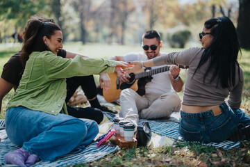 Wall Mural - A joyful group of friends having a fun picnic in the park, playing guitar and creating lasting memories in a natural, sunny setting.