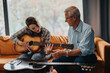 © qunica.com - An elderly professor guides a student in learning guitar techniques during a music class in a school. The lesson takes place in a relaxed and supportive environment.