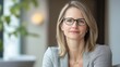 © munirahsamsudin - Professional woman with glasses in modern office setting, embodying confidence and elegance while sitting at a table, with natural light and greenery in the background.