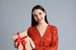 © New Africa - Woman in red dress holding Christmas gift on grey background