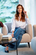 © sepy - Portrait of an attractive woman wearing white shirt and jeans and relaxing in an armchair in a modern home