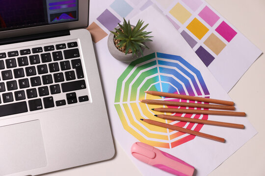 Designer's workplace with laptop, stationery and palettes on white table, flat lay