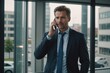 © ThomasLENNE - Confident Businessman talking on cell phone at office window
