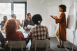 © NDABCREATIVITY - Happy african american female leader holding negotiations meeting with friendly diverse colleague