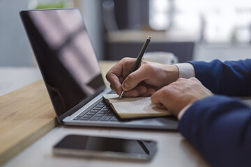 Aufkleber - A man's hand inscribing in a notepad on a modern laptop, captured closely, with a vague background