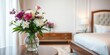 © OneWayPhoto - Fresh bouquet of flowers in a vase on a stylish white nightstand table in a glamorous bedroom interior with a king size bed, vase, wooden