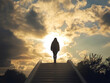 © Chatupat - Silhouette of person ascending stairs with dramatic clouds.