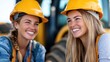 © LifeMedia - Two young women construction workers laughing joyfully while sitting at a job site with machinery in the background, conveying happiness and friendship.