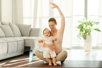 Young mother workout with her baby girl, sitting together on yoga mat. Sport and motherhood concept