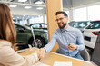 © Dusan Petkovic - Buyer with car keys and saleswoman sitting in car showroom and shaking hands while closing the deal.