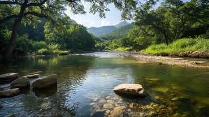 Aufkleber - A serene river flows through lush greenery, framed by mountains under a clear blue sky, creating a tranquil natural landscape.