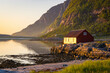 © Travel 'n' Lifestyle - View of serene fishing house by the calm coast at sunset with mountains in the background, Bodo, Norway.