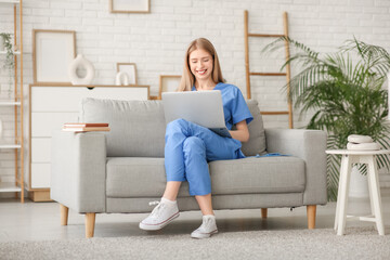 Wall Mural - Female medical intern with laptop on sofa in living room