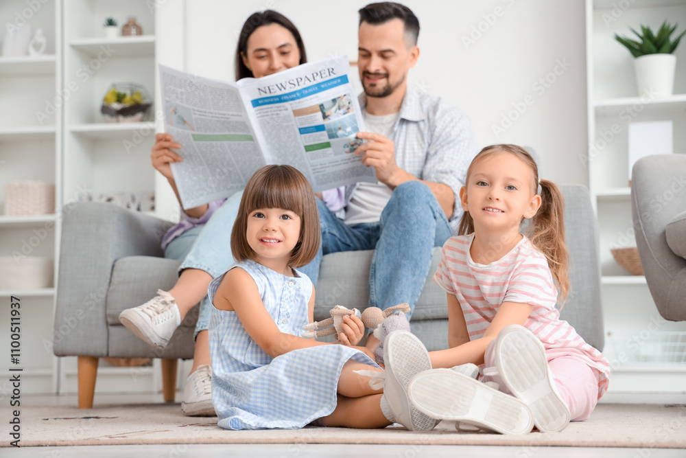 Happy sisters playing with toy while their parents reading newspaper on sofa at home
