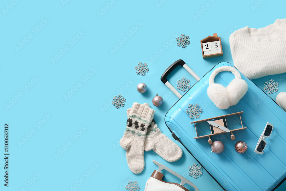 Suitcase with winter clothes and Christmas decor on blue background. Top view