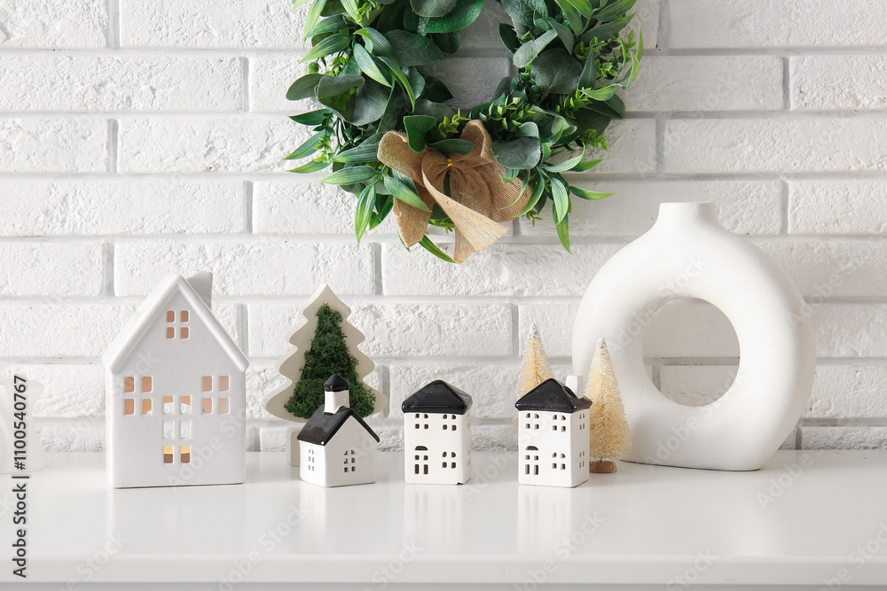 House shaped candle holders with Christmas trees on table near white brick wall