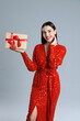 © New Africa - Woman in red dress holding Christmas gift on grey background