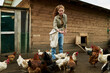 © pressmaster - Female farmer with sack of oat feeding bred hens while standing by wooden coop in the yard of livestock farm