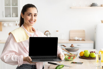 Aufkleber - Cheerful Young Lady Showing Empty Laptop Screen Posing Standing In Modern Kitchen At Home. Smiling Woman Recommending Cooking Application Or Website With Healthy Online Recipes. Mockup