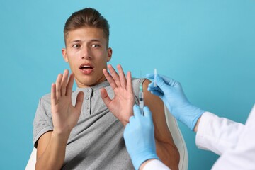 Wall Mural - Needle phobia. Scared man making stop gesture near doctor with syringe and vial on light blue background