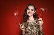 © New Africa - Smiling woman with sparklers celebrating Christmas on red background