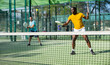 © JackF - Sporty african american man padel tennis player trains on the court with a partner using a racket to hit the ball