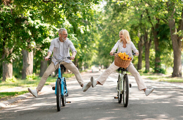 active retirement. happy senior couple having fun while riding bicycles at summer park, cheerful mat