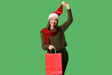 Wall Mural - Young woman in Santa hat with shopping bag on green background