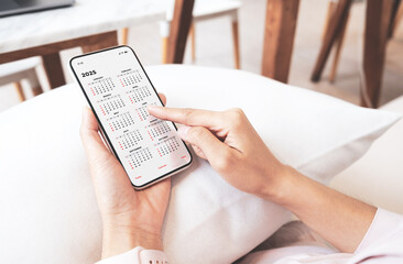 Businesswoman using smartphone with monthly calendar to plan 2025 activities. Scheduling and organizing plans. Technology and business concept.