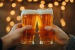 © Preeyanuch - Two hands clinking glasses of beer in a celebratory atmosphere with warm bokeh lights in the background.