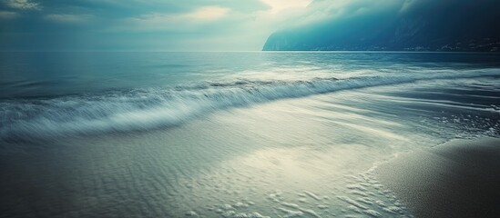 Poster - Tranquil coastal scenery showcasing serene waves, smooth sandy beach, and dramatic land forms under a moody sky.