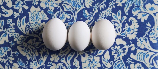 Poster - Top view of three white eggs arranged in a row on a vibrant blue floral patterned napkinèƒŒæ™¯