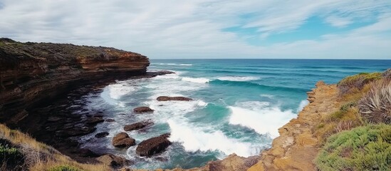 Poster - Coastal landscape with large waves crashing on rocky shoreline under a vibrant sky and lush greenery in the foreground.