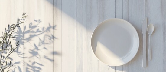 Poster - Minimalist setup of an empty white plate with fork and spoon on a textured wooden surface illuminated by soft natural light