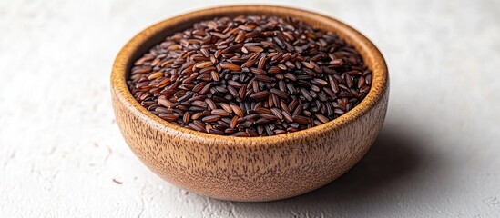 Aufkleber - Bowl of uncooked black rice in a wooden bowl on a white surface viewed from above showcasing its texture and color.