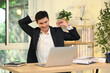 © Prathankarnpap - Smiling adult businessman stretching his arms while sitting at desk relaxing during a busy workday